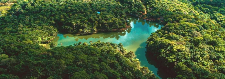Aerial drone view of a serene blue lake nestled deep inside a lush green tropical forest at Hola Africa.